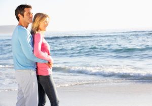 Young Couple Standing On Sandy Beach Looking Out To Sea